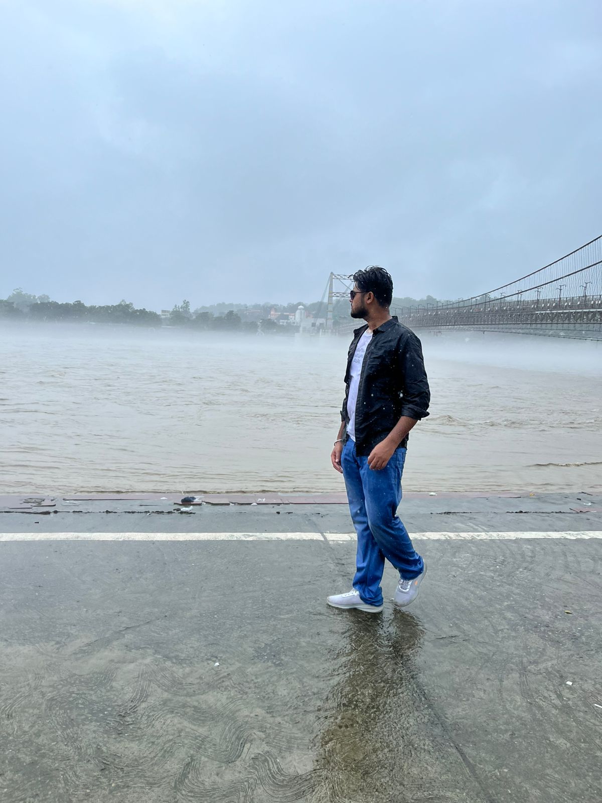 Niraj Aarya walking beside a river bridge